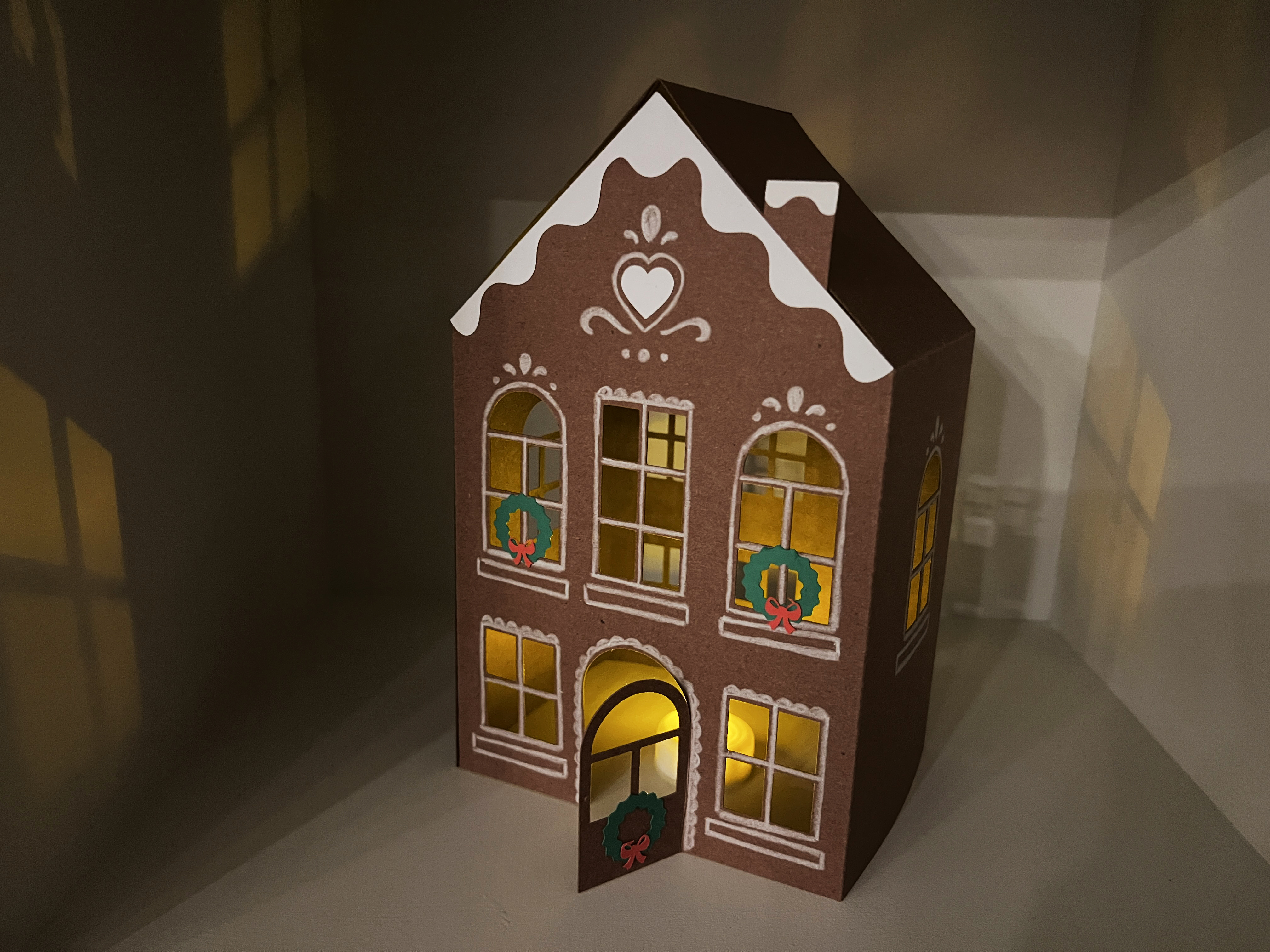 The image shows a lighted model of a dark brown building decorated with white trimming and two wreaths